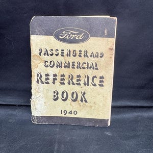Op de afbeelding: Een vintage Ford Passenger and Commercial Reference Book uit 1940. De omslag is bruin met zwarte tekst en het Ford-logo. Het boek vertoont tekenen van slijtage.