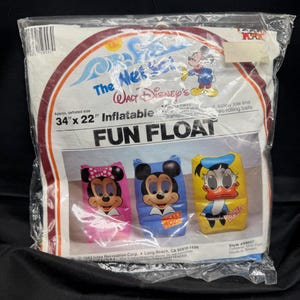 May include: Sealed package of a Walt Disney's Fun Float. The inflatable float features Minnie Mouse, Mickey Mouse, and Donald Duck. The package reads "34" x 22" Inflatable". The package is clear plastic with a white and red border.