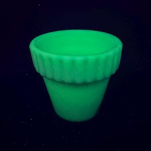 Op de afbeelding: Een kleine, groene bloempot met een geribbelde rand. De pot heeft een klassieke vorm, breder aan de bovenkant en taps toelopend naar de basis. De pot is gemaakt van een solide, ondoorzichtig materiaal. Vintage bloempot.