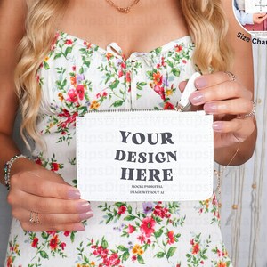 Può includere: Una pochette bianca con cerniera con il testo "YOUR DESIGN HERE" in nero. La pochette è tenuta da una persona che indossa un abito bianco a fiori.