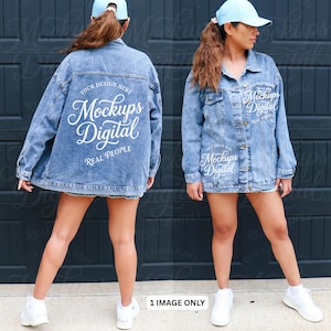 May include: Light blue denim jacket with the text "Mockups Digital" on the back and front. The jacket has a classic button-up design and is worn with a light blue baseball cap and white sneakers. The text "Real People" is also visible.
