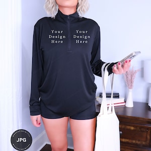 Puede incluir: Camiseta negra de cuello alto y manga larga con cremallera. La camiseta tiene el texto "Your Design Here" en la parte delantera.