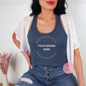 Op de afbeelding: Een vrouw draagt een blauw tanktop met de tekst "MOCKUPS DIGITAL YOUR DESIGN HERE MOCKUPS DIGITAL" erop gedrukt. Ze draagt ook een wit vest en een blauwe jeans.