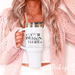 May include: White stainless steel tumbler with a black and white design that says "YOUR DESIGN HERE". The tumbler has a lid and a straw. The tumbler is being held by a person wearing a pink sweater.