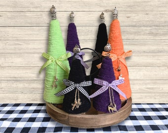 May include: Five Halloween-themed mini trees made from towels, decorated with black and white checked ribbon, and various Halloween charms. The trees are arranged on a wooden tray with a checkered tablecloth in the background.