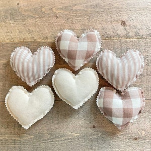 May include: Six heart-shaped fabric pillows in various patterns. Two are white with a subtle texture, two are brown and white gingham, and two are brown and white striped.