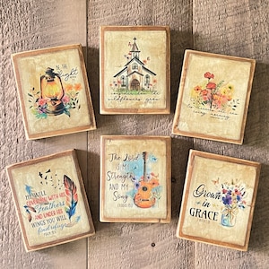 May include: Six wooden signs with inspirational quotes and floral designs. The signs feature quotes such as "Be the light", "He will cover you with his feathers", "The Lord is my strength and my song", "Consider how the wildflowers grow", "He refreshes me every morning", and "Grown in grace".