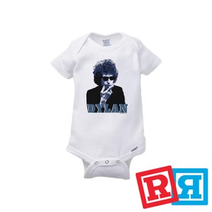 May include: White baby onesie with a blue and white image of Bob Dylan, with the word "DYLAN" printed in blue below the image.