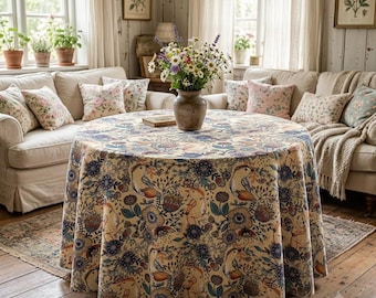 May include: A round tablecloth featuring a cream-colored base with a repeating pattern of stylized birds, dark blue flowers, and orange botanical elements. A ceramic vase filled with a bouquet of wildflowers sits on the center of the table.