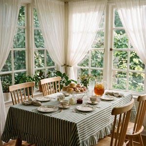 May include: A dining table set with a green and white striped tablecloth featuring a ruffled edge. The table holds a tiered stand of scones, a glass pitcher of iced tea, floral teacups, saucers, and small jars of jam and cream.