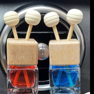 Op de afbeelding: Twee autoluchtverfrissers met houten bovenkanten en witte bolvormige diffusers. De luchtverfrissers zijn gevuld met rode en blauwe vloeistof.