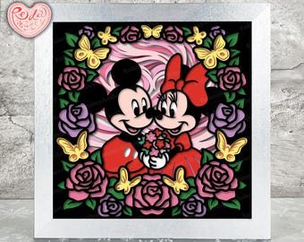 Puede incluir: Una caja de sombra de papel con Mickey Mouse y Minnie Mouse sosteniendo un ramo de flores. Los personajes están rodeados de rosas rosas y rojas, hojas verdes y mariposas.