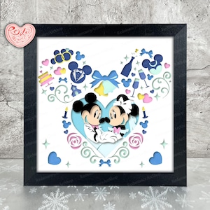 Puede incluir: Una obra de arte en papel recortado enmarcada con Mickey y Minnie Mouse en una temática de boda. La obra incluye elementos azules, rosas y blancos, como corazones y lazos, todo dentro de un marco negro.