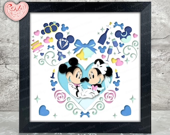 Puede incluir: Una obra de arte en papel recortado enmarcada con Mickey y Minnie Mouse en una temática de boda. La obra incluye elementos azules, rosas y blancos, como corazones y lazos, todo dentro de un marco negro.