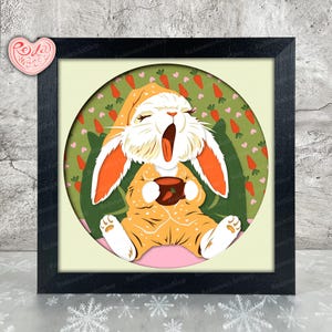 May include: A framed art print featuring a yawning bunny in orange pajamas holding a cup. The bunny is set against a green background with carrot and heart patterns. The frame is black, and the artwork is labeled "Redamancy ArtShop".