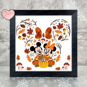 May include: A framed print featuring Mickey and Minnie Mouse in a fall-themed design. The artwork includes pumpkins, autumn leaves, acorns, and mushrooms, with Mickey and Minnie embracing. The frame is black.