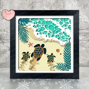 May include: A framed paper art piece showing a beach scene with three turtles heading towards the sea. The artwork uses layers of paper in blue, green, beige, and white, creating a 3D effect. A starfish and seashells are also visible.