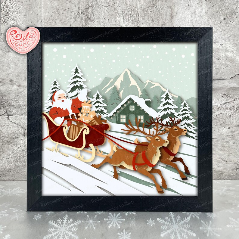 May include: A framed paper art piece depicting Santa Claus in a sleigh pulled by reindeer, set against a snowy winter landscape with a house and trees. The artwork is in a black frame and features the text "Redamancy ArtShop".