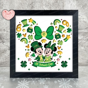 May include: A framed paper craft featuring Mickey Mouse and Minnie Mouse dressed in green shamrock-themed outfits. The background is a white paper with green shamrocks, gold coins, and rainbows cut out. The text "St. Patrick's Day" is at the bottom of the frame.