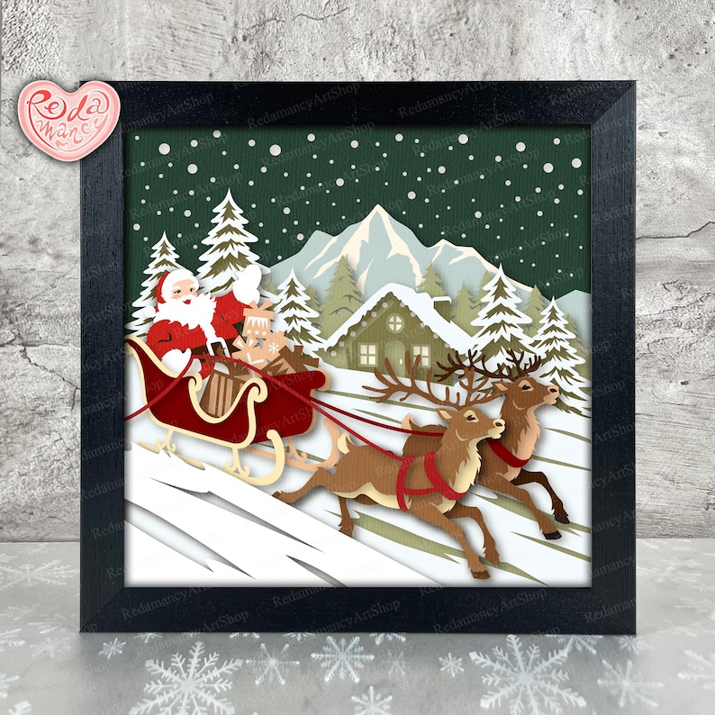 May include: A framed paper art piece depicting Santa Claus in a red sleigh pulled by two reindeer, set against a snowy winter landscape with a cabin and pine trees. The artwork is in a black frame.