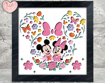Puede incluir: Un diseño de corte de papel enmarcado con Mickey y Minnie Mouse rodeados de flores rosas, amarillas y verdes. El diseño está en un marco negro.