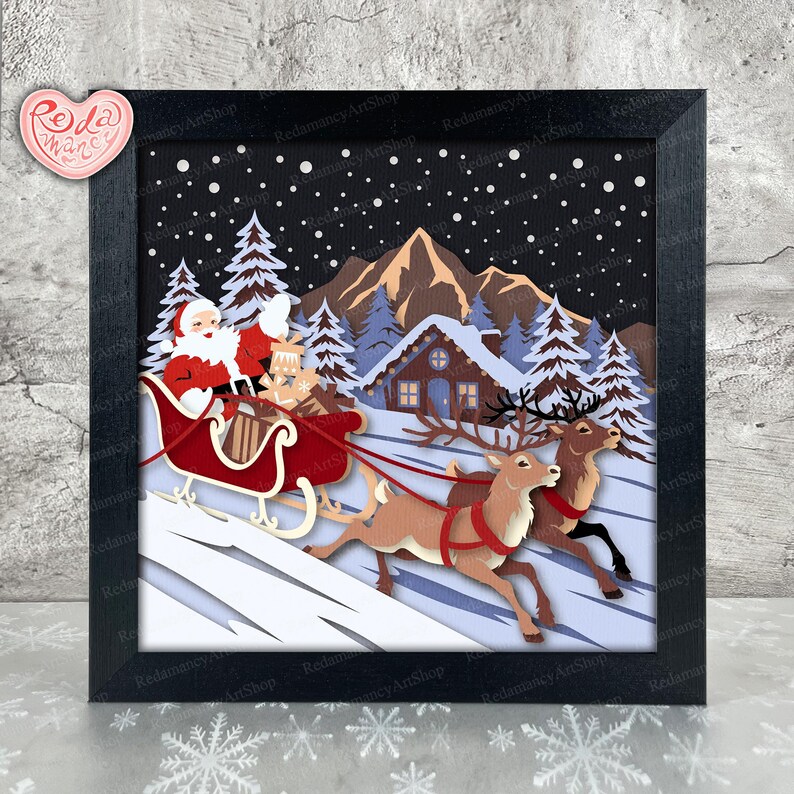 May include: A framed paper art piece depicting Santa Claus in a red sleigh pulled by reindeer, flying over a snowy landscape with a cabin and pine trees. The artwork is in a black frame, with the text "Redamancy ArtShop" visible.