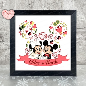 May include: Framed artwork depicting Mickey and Minnie Mouse, their heads shaped as mouse ears, filled with hearts, roses, and musical notes. A banner below reads "Chloe & Noah". The artwork is presented in a black frame.