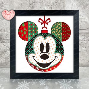 May include: Framed Christmas ornament featuring Mickey Mouse's face. The ornament has a red bow and is decorated with festive patterns in red, green, and gold. The frame is black, and the artwork is displayed on a white background.