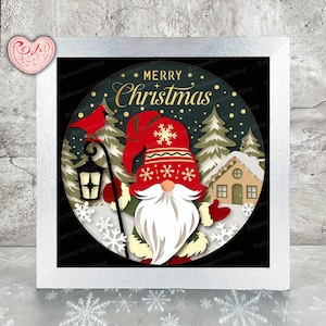 May include: A framed Christmas artwork depicting a gnome with a white beard and a red hat. The image includes a house, trees, and the words "MERRY CHRISTMAS". The background is dark green with white snowflakes.