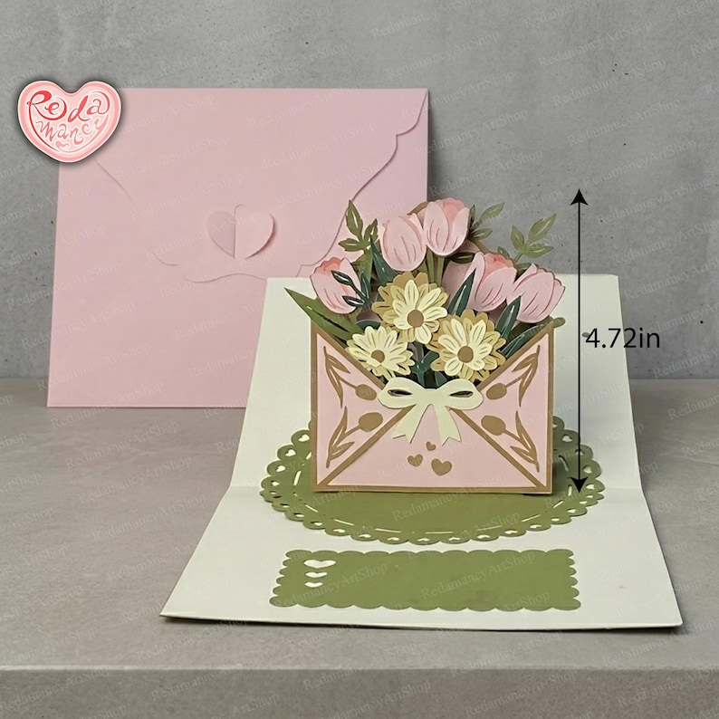 May include: A pink pop-up card featuring a bouquet of pink tulips and yellow daisies emerging from a decorative envelope. The card is 12 cm tall and includes a matching pink envelope.