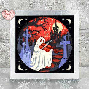 Puede incluir: Una obra de arte en papel en capas que presenta un fantasma blanco tocando un violín rojo en una escena de cementerio espeluznante. El fondo incluye un cielo rojo, una casa embrujada y notas musicales. La obra está enmarcada en un cuadrado blanco.