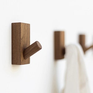 May include: Three wooden wall hooks with a simple design. The hooks are made of dark brown wood and have a rectangular base with a single hook extending out.