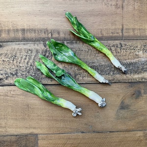 May include: Four ceramic green onions, each with a white bulb at the base, are arranged on a wooden surface.