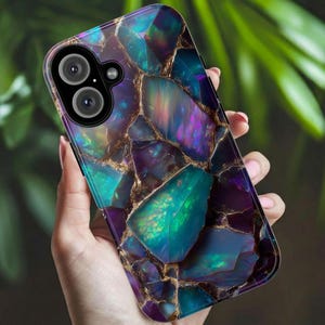May include: A smartphone case with a vibrant, gemstone-like design. The case features a mosaic of teal, purple, and gold-colored sections, creating a unique and eye-catching pattern. The case has a camera cutout and is held in a hand.