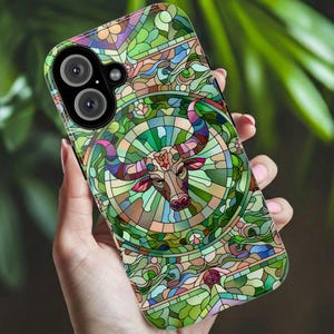 May include: A smartphone case featuring a stained-glass design with a bull illustration. The case has a green, brown, and purple color scheme. The bull is centered within a circular design, surrounded by intricate patterns.