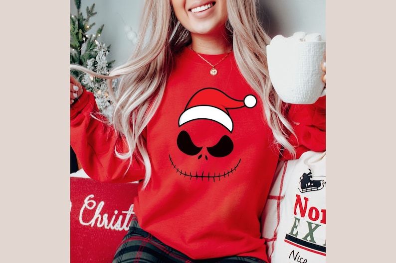 May include: Red Christmas sweater with a black and white Jack Skellington face wearing a Santa hat. The sweater has long sleeves.