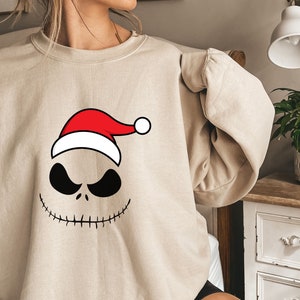May include: A beige sweatshirt with a black and white illustration of Jack Skellington from The Nightmare Before Christmas wearing a red and white Santa hat.