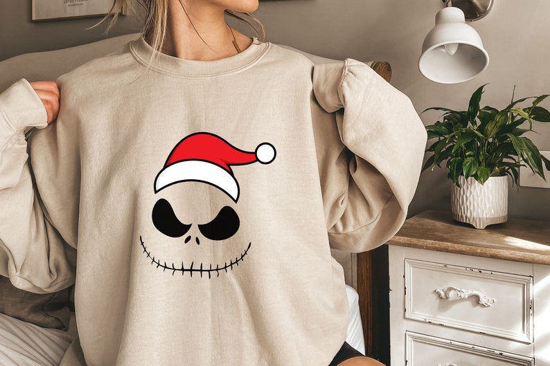 May include: A beige sweatshirt with a black and white illustration of Jack Skellington from The Nightmare Before Christmas wearing a red and white Santa hat.