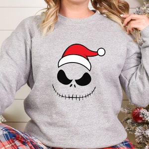 May include: A gray sweatshirt with a black and white Jack Skellington face wearing a red Santa hat.
