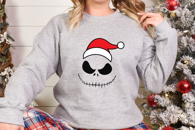 May include: A gray sweatshirt with a black and white Jack Skellington face wearing a red Santa hat.