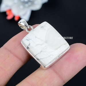 May include: A square, white howlite pendant with a silver bail. The stone has gray veining and is set in a silver bezel. The pendant is held by a person's fingers against a dark background. The text "STSILVERSTORE" is visible on the pendant.