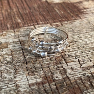May include: A silver ring with multiple bands and small round beads. The ring is on a wooden surface.