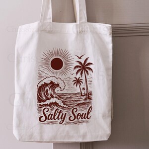 May include: A white canvas tote bag with a brown graphic of a sun, palm trees, and a wave. The text "Salty Soul" is printed below the graphic.