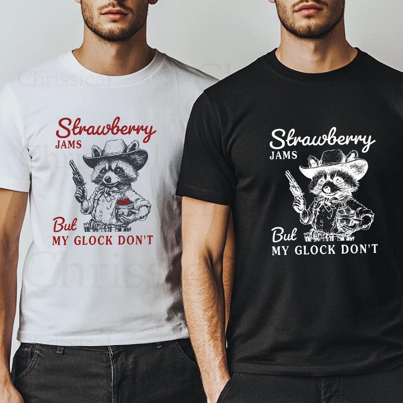 May include: Two t-shirts featuring a graphic of a raccoon wearing a cowboy hat and holding a gun. The text on the shirts reads "Strawberry Jams But My Glock Don't".