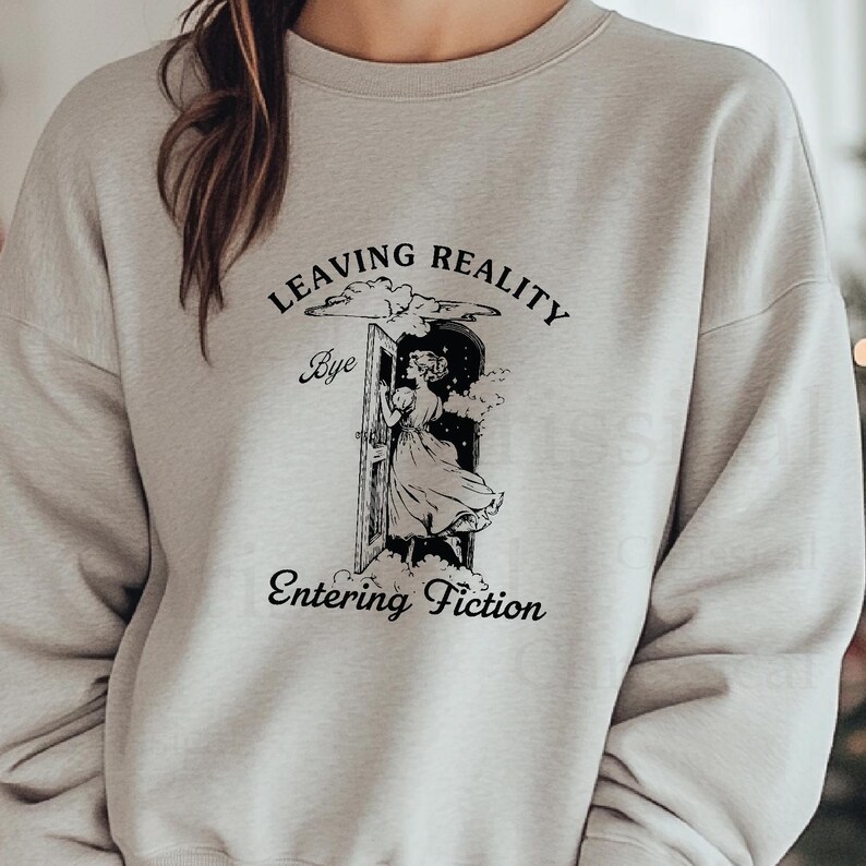 May include: A gray sweatshirt with a black graphic print of a woman stepping through a door with the text "Leaving Reality Bye Entering Fiction".