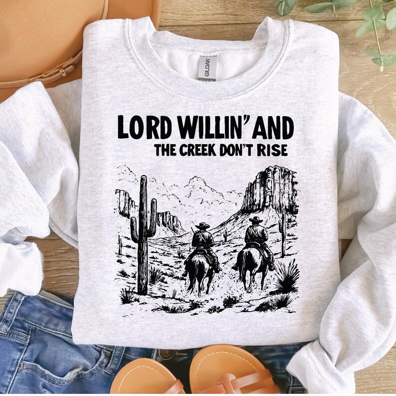 May include: A gray sweatshirt with a black graphic print of two cowboys riding horses. The text "Lord Willin' and the Creek Don't Rise" is printed on the sweatshirt.
