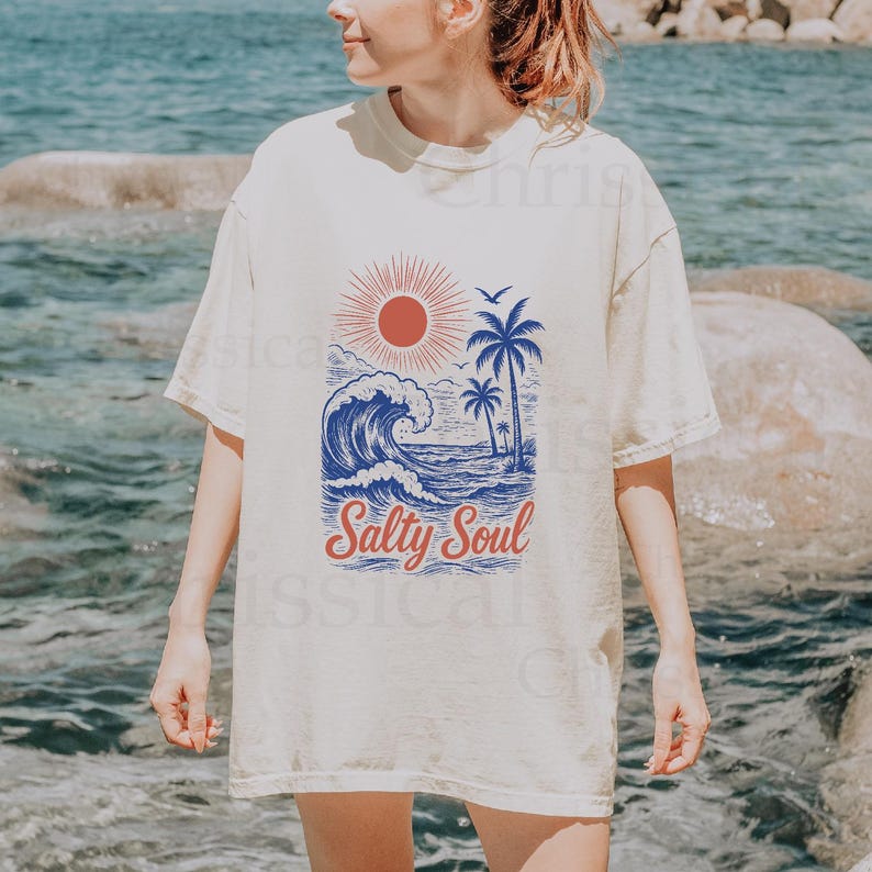 May include: A white t-shirt with a vintage-style graphic of a palm tree, sun, and wave. The text "Salty Soul" is printed in red and blue below the graphic.
