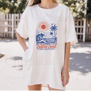 May include: White oversized t-shirt with a graphic of a blue wave, palm trees, and a red sun. The text "Salty Soul" is printed in red and blue below the graphic.