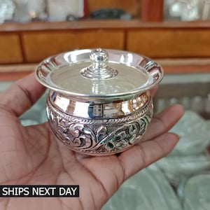 May include: A silver container with a lid, featuring intricate floral designs. The container is round and has a smooth, polished finish.