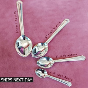 May include: Four silver spoons of varying sizes, approximately 6, 5, 4, and 2.8 inches long, are arranged on a maroon surface. Each spoon has a decorative handle and a reflective bowl. The text "SHIPS NEXT DAY" is visible.
